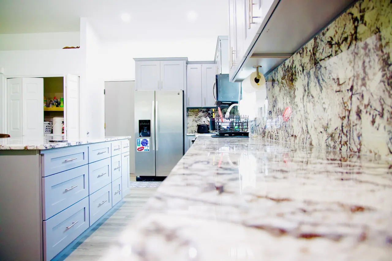Modern kitchen with granite countertops, gray cabinets, stainless steel appliances, and light wood flooring.