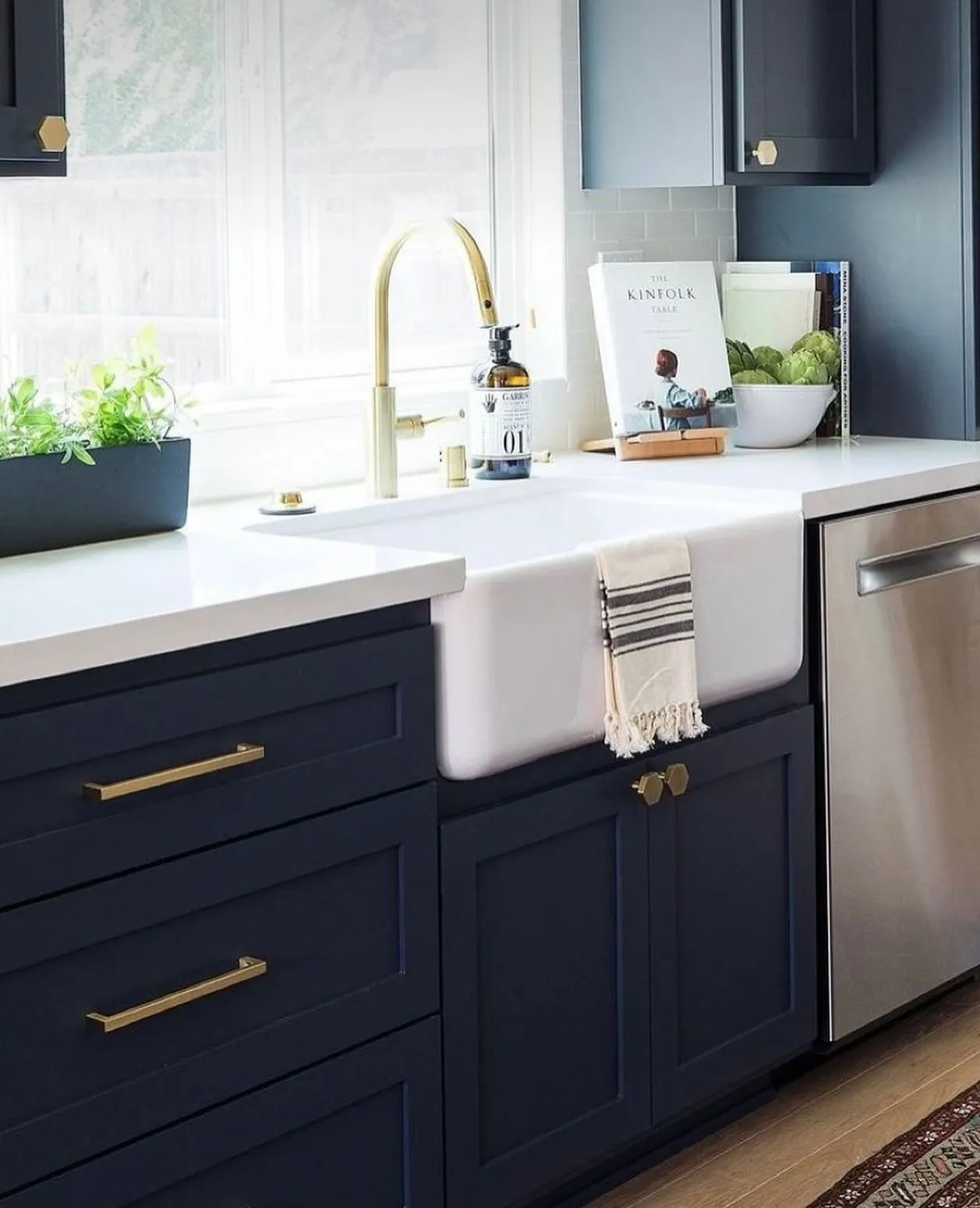 Navy blue kitchen cabinets with gold handles, a white sink, a gold faucet, a white countertop and a steel dishwasher.